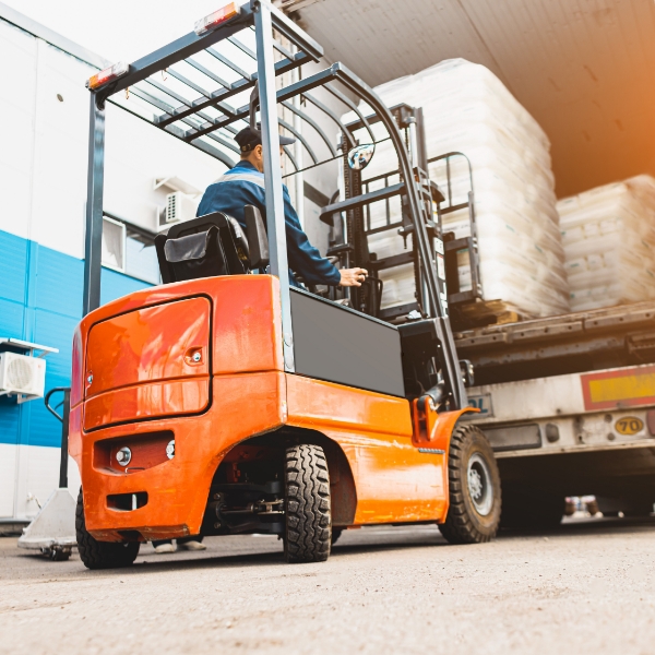 A man driving a forklift to load pallets onto a box truck.